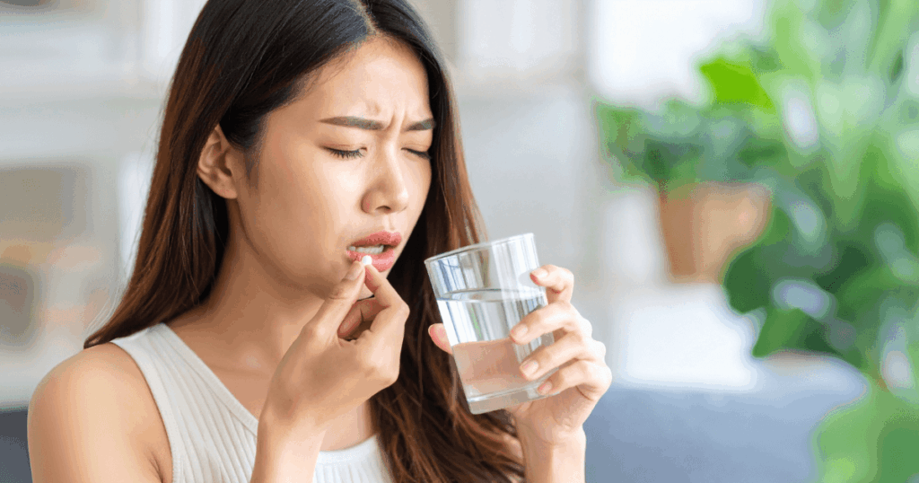 歯の痛みをやわらげるために鎮痛剤を飲む女性