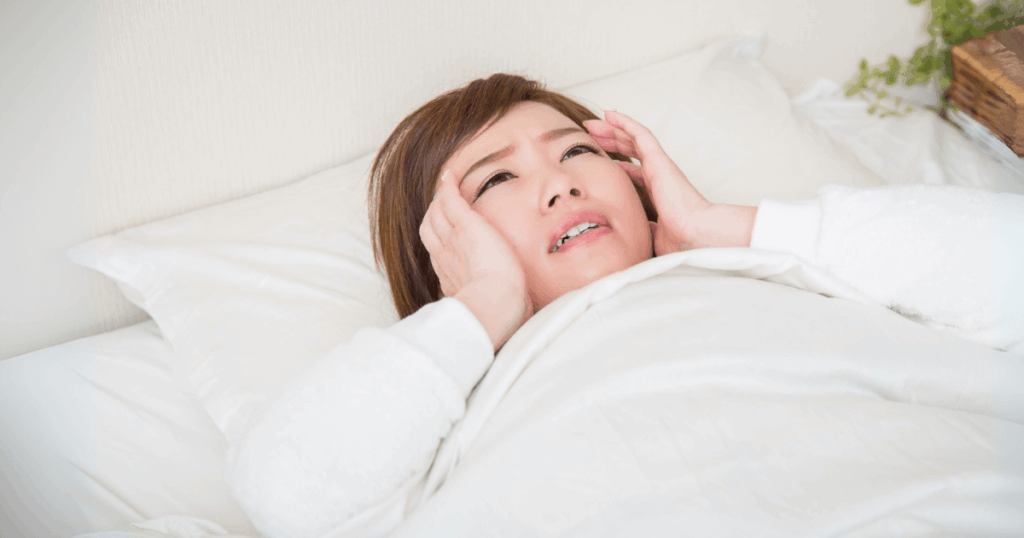 夜に布団の中で歯の痛みに苦しむ女性