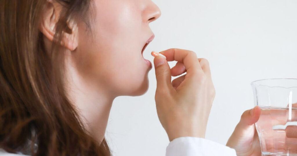 鎮痛薬を水と一緒に服用する女性