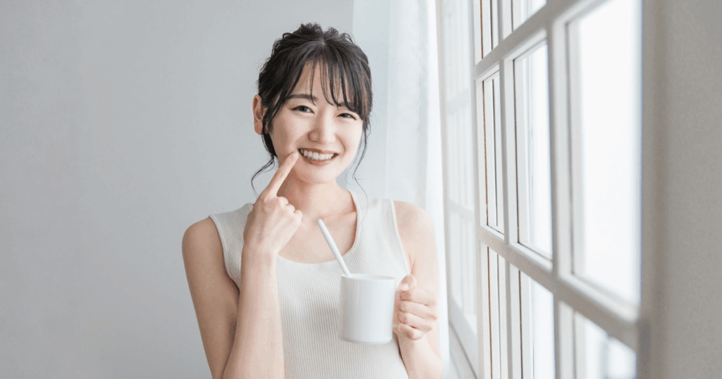 虫歯予防のために歯みがきを行い、口元を指して笑顔を見せる女性のイメージ
