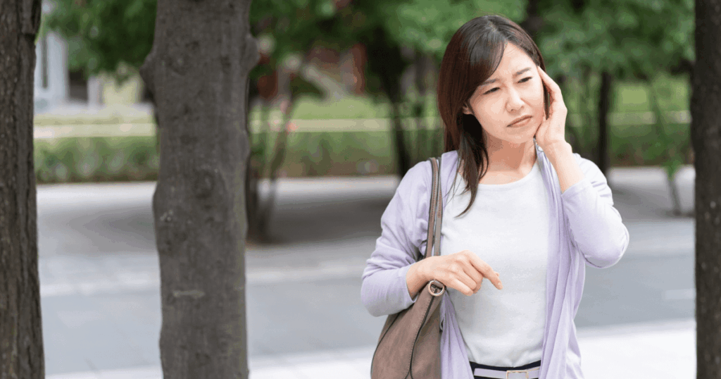 外出中に頬を押さえて歯の神経の痛みを感じている女性