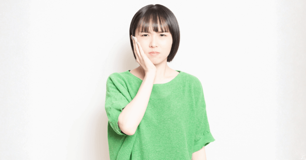 抜歯後の痛みを感じて頬を押さえる女性のイメージ