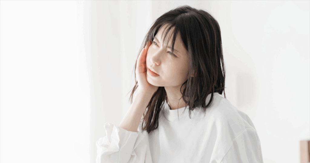 歯と歯の間が痛くて頬に手を当てる女性。虫歯や歯ぐきの炎症による痛みを表すイメージ。