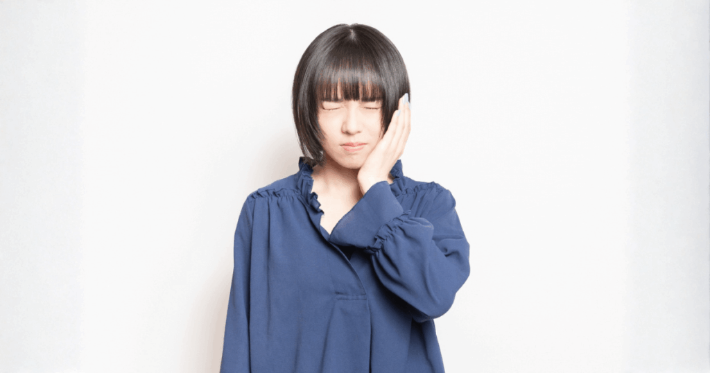 歯が痛くて頬に手を当てる女性。抜歯が必要か迷っている状況のイメージ