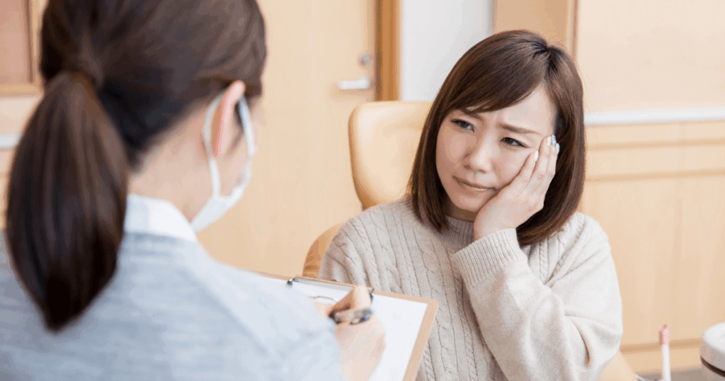 頬の痛みを訴えて歯科医に相談する女性