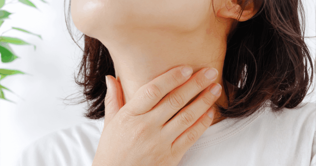 抜歯後に喉の痛みを感じて首元に手を当てている女性の写真