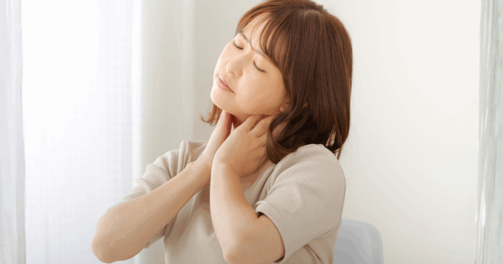 喉の痛みで首元を押さえ不調を感じる女性