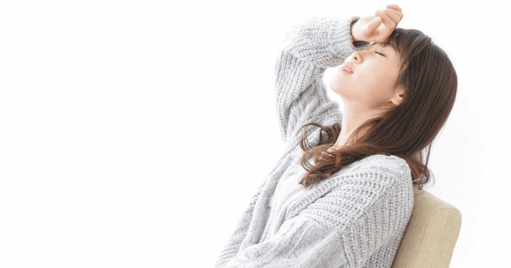 体調不良で額に手を当ててつらそうにしている女性