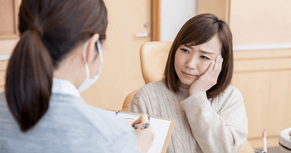 歯の痛みを訴える女性が歯科医院で相談している様子の写真。