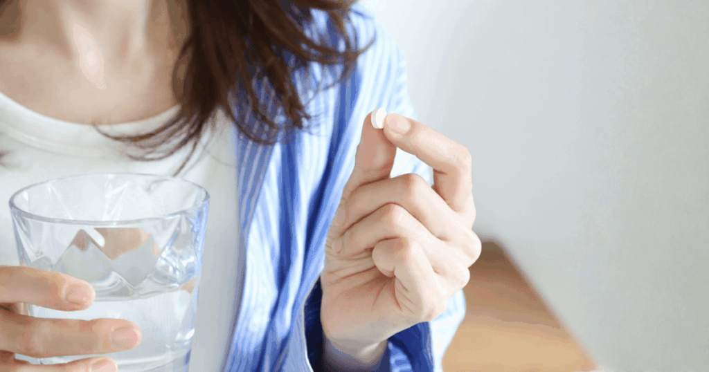 痛み止めの錠剤を水と一緒に飲もうとしている女性の手元