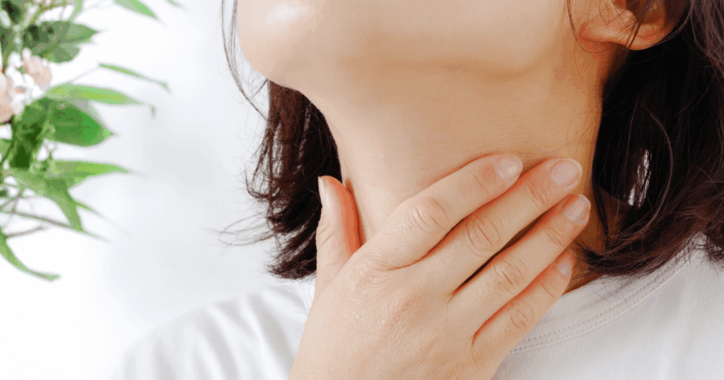 抜歯後の喉の痛みや違和感を確かめるように喉へ手を当てている人の写真