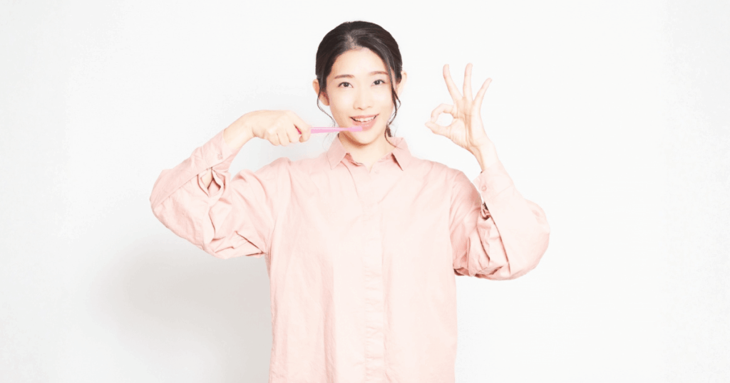 歯みがきをしながら笑顔でOKサインをする女性の写真