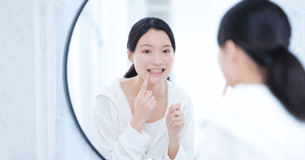 親知らず抜歯後の穴に食べかすが詰まっていないか口元を鏡で確認しているイメージ画像