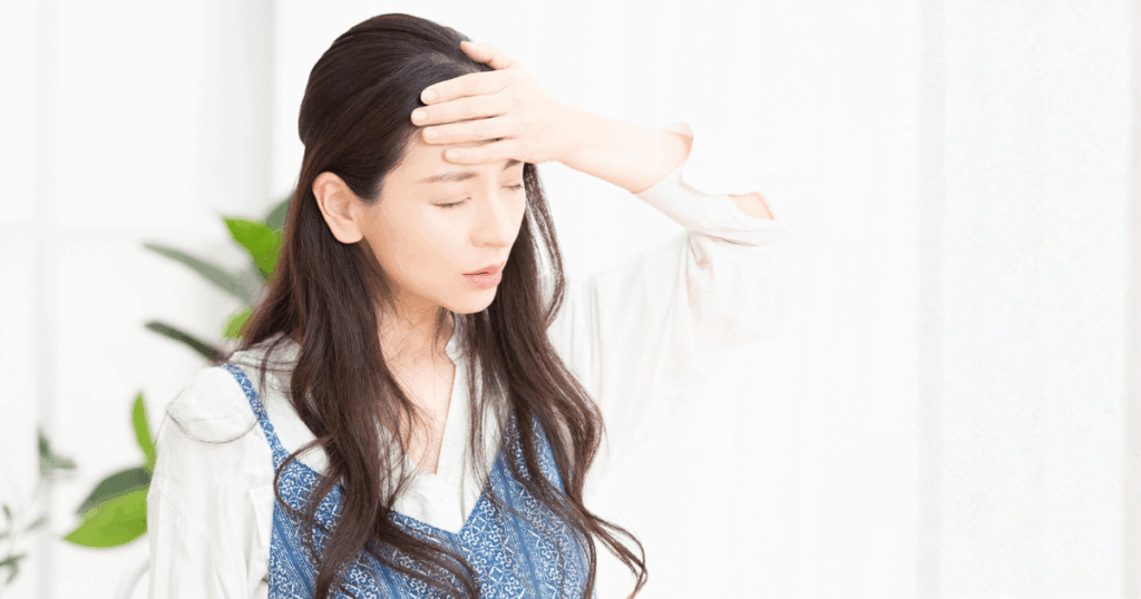 歯の痛みと頭痛に加えて体調不良を感じ、額を押さえている女性