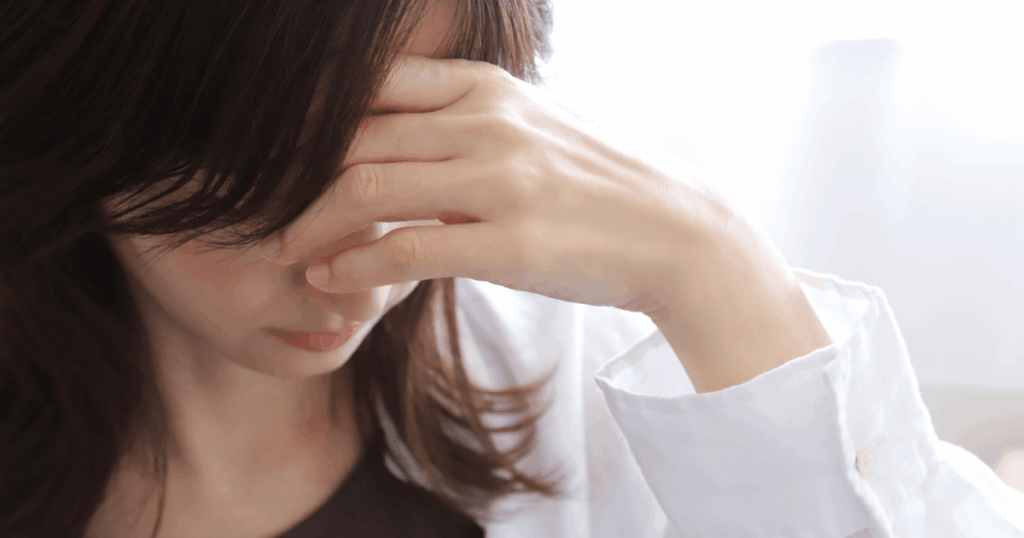 歯の痛みと頭痛が重なり、こめかみを押さえてつらそうにしている女性