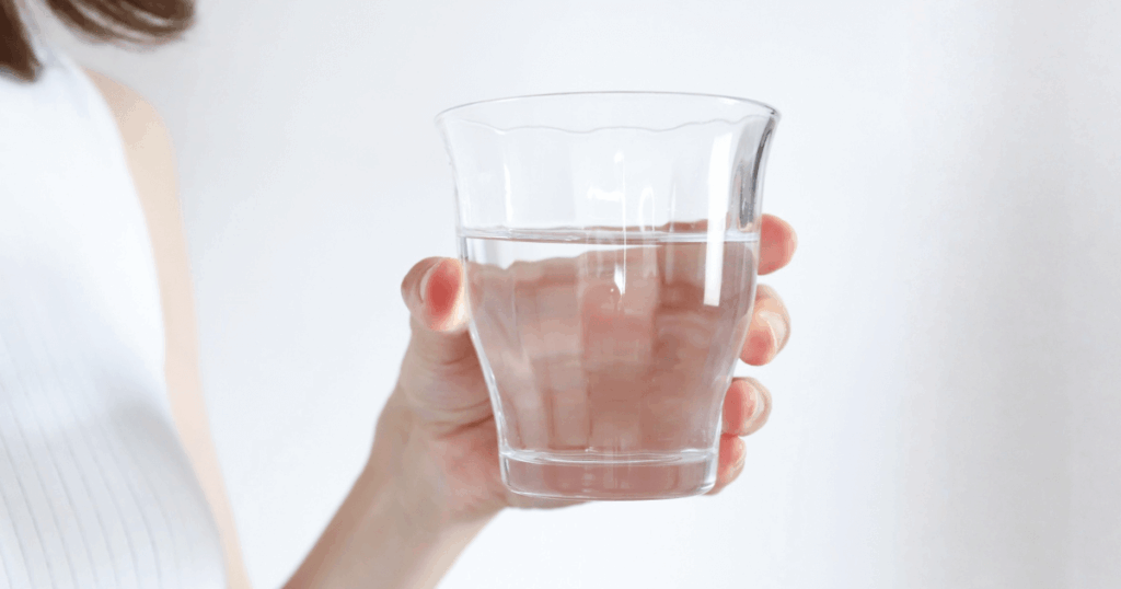 コップの水を持つ手元の写真（歯周病とうがいのイメージ）